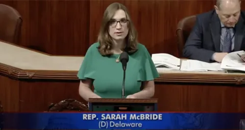 Rep. McBride in a green dress on the well of the House of Representatives